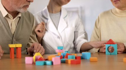 Senior man and woman combining color building blocks on table, dementia therapy