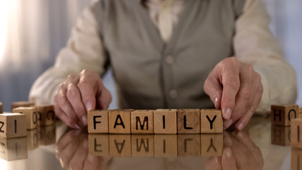 Male pensioner making word family of wooden cubes on table, old age loneliness