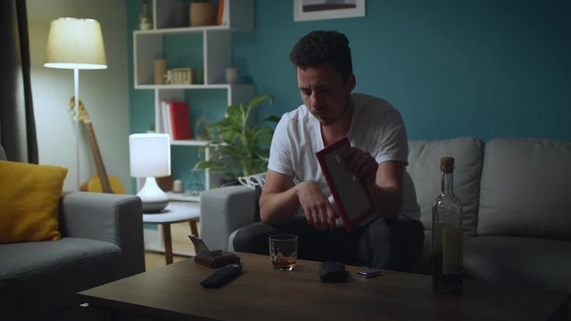 Sad man looking at photo of ex-girlfriend, regretting break-up and drink alcohol