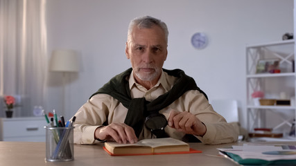 Pensioner with magnifying glass looking at camera, reading book, leisure time