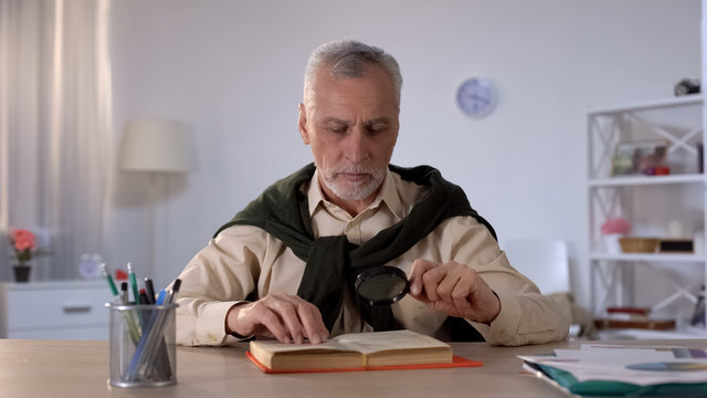 Senior man reading book with magnifying glass, attention to details, erudition