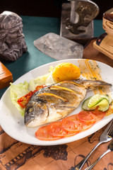 delicious roasted dorado or sea bream fish with orange slices on white plate on old map background