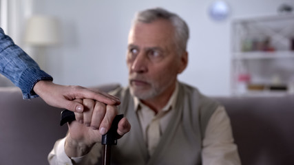 Female hand comforting old man leaning on stick, hospice care for disabled
