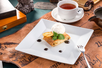 Freshly baked apple strudel with vanilla ice cream and mint and cup of tea on old map background