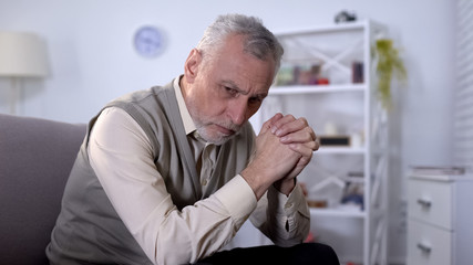 Fototapeta premium Depressed senior man sitting on coach and thinking about life problems, ptsd