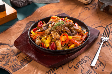 Beef fajitas with colorful vegetables in pan on old map background