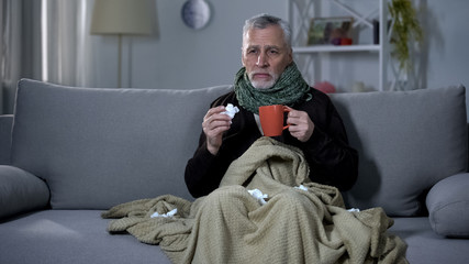 Ill pensioner sneezing and holding hot beverage, treating influenza, epidemic