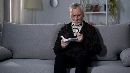 Old man reading instruction for pills with magnifier, treating vision impairment