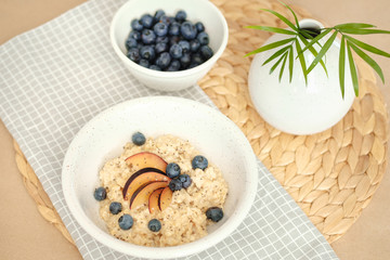porridge with blueberries, plums and chia seeds in a ceramic bowl on a wicker stand.