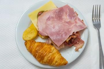 European breakfast meal with croissant and ham on white plate