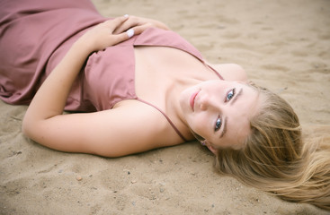 Young woman in pink dress lying on the sand and enjoys sea.