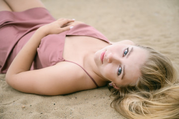 Young woman in pink dress lying on the sand and enjoys sea.