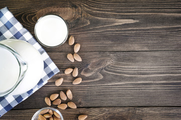 Fresh almond milk in glass and pitcher on dark wooden table. Rustic style.