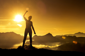 Frau in Siegerpose bei Sonnenaufgang auf einem Berggipfel