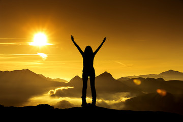 Frau in Siegerpose bei Sonnenaufgang auf einem Berggipfel