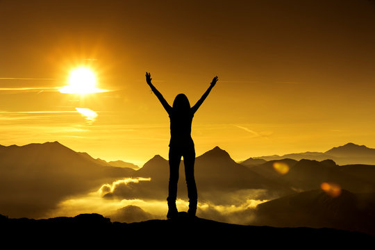 Frau in Siegerpose bei Sonnenaufgang auf einem Berggipfel