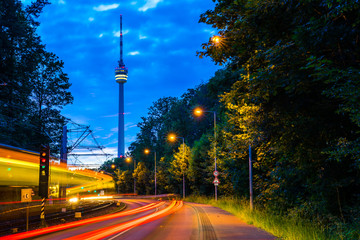 Germany, Lights of illuminated train and traffic passing by street road to television tower of...