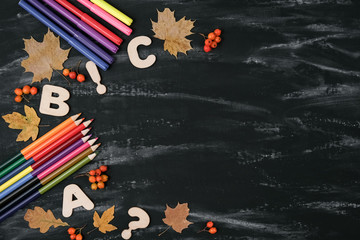 Back to school concept. School equipment with colored pencils, dried maple leaves on black table background. Flat lay, top view, copy space.