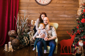 Happy family portrait on Christmas, mother, father and son sitting on highchair at home, chritmas decoration and presents around them