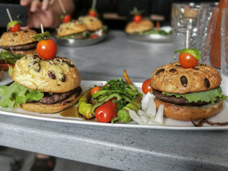 Beef burgers with cherry tomatoes on top with vegetables beside closeup.