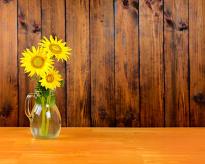 Sunflower flowers in a vase on the table. Brown wooden planks background.