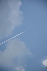 The plane soars up against the blue sky with clouds