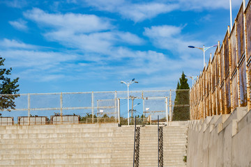 Outdoor blue sky with white clouds and cement stands and iron fence