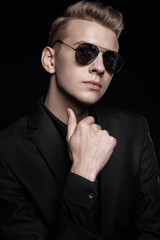 young man with black glasses in black jacket on black background,