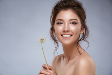 attractive girl with perfect skin and naked shoulders holding dandelion and smiling