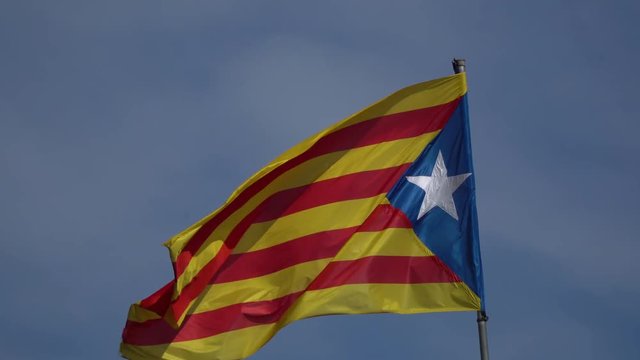 The flag of Catalonia waving in the wind on a background of blue sky.