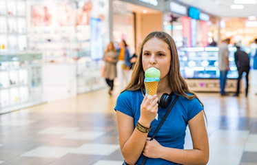 portrait of young teenager brunette girl with long hair eating tasty cone ice cream in shopping mall