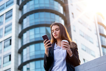 Attorney - young woman lawyer looking at mobile smartphone and drinking coffee from disposable paper cup. Young business woman professional in the city