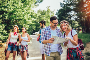Group of smiling friends walking with backpacks in woods - adventure, travel, tourism, hike and people concept