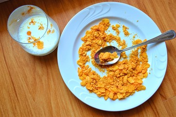 plate of cornflakes and a spoon on it, and a glass of milk standing next to it on the table 