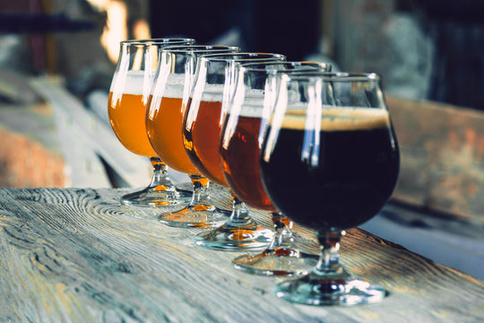 Glasses of different kinds of dark and light beer on wooden table in line. Cold delicious drinks are prepared for a big friend's party. Concept of drinks, fun, meeting, oktoberfest.