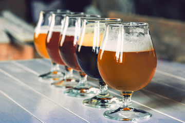 Glasses of different kinds of dark and light beer on wooden table in line. Cold delicious drinks are prepared for a big friend's party. Concept of drinks, fun, meeting, oktoberfest.