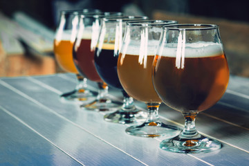 Glasses of different kinds of dark and light beer on wooden table in line. Cold delicious drinks are prepared for a big friend's party. Concept of drinks, fun, meeting, oktoberfest.