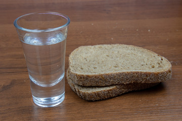 A glass of vodka and sliced ​​black bread on a wooden table