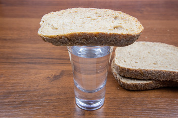 A glass of vodka and sliced ​​black bread on a wooden table