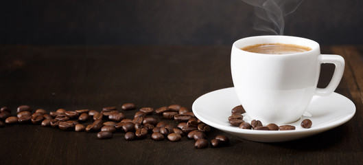 A cup of coffee and coffee beans on the table. Black background.