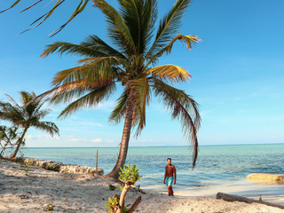 Fototapeta na wymiar Man walking on the white beach and turquoise water with clear blue sky and lots of palm trees on Sicsican Island in Balabac, Palawan, Philippines