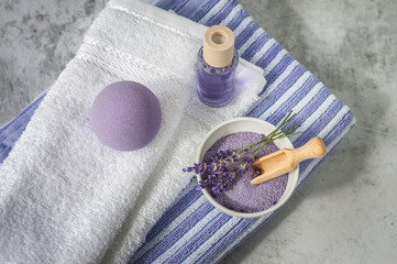 Stack of clean soft towels with lavender, air freshener and bath salt on light gray background. Spa towels against a textured wall. Minimalism, soft focus, top view.