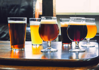 Glasses of different kinds of dark and light beer on wooden table in line. Cold delicious drinks are prepared for a big friend's party. Concept of drinks, fun, meeting, oktoberfest.