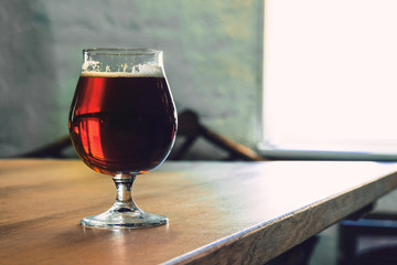 Glass of dark beer on wooden table against brick background. Cold delicious drink is prepared for a friend's party. Concept of drinks, fun, meeting, oktoberfest. Copyspace.