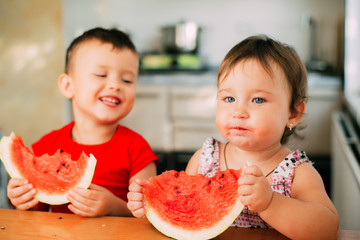 Children, brother and sister, boy and girl in the kitchen eating watermelon, a lot of fun