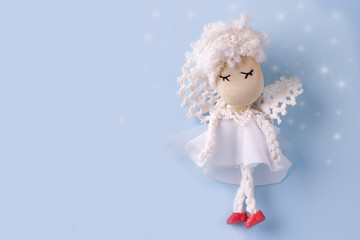 Postcard layout with a cute handmade angel in white clothes on a light blue background with bokeh. Copy space