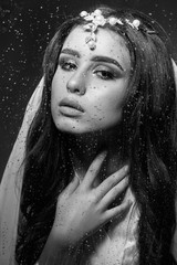 Beautiful young girl bride. It rains dripping down the glass.  Fashion girl of Caucasian appearance posing. Sexy makeup and perfect hair curls. Drops on the glass. Black and white.