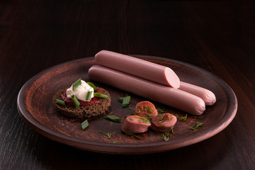 Sausage on a dark background in the plate and on the cutting board. Sausage with sauces and snacks. Onions, garlic, parsley, dill, olives, cheese, tomatoes, cucumbers, basil, eggs with sausage.