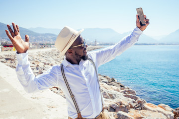 handsome african american person casual fashion look outfit in straw hat,white shirt walking by Tyrkey coast making selfie photo portrait on smartphone camera