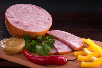Sausage on a dark background in the plate and on the cutting board. Sausage with sauces and snacks. Onions, garlic, parsley, dill, olives, cheese, tomatoes, cucumbers, basil, eggs with sausage.